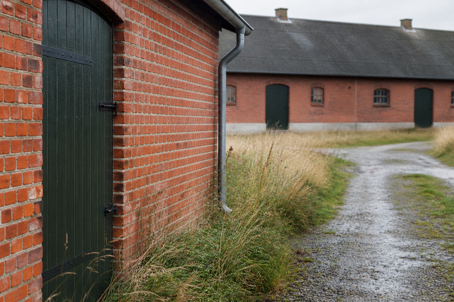 Røde landbrugsbygninger med grønne porte og grusvej